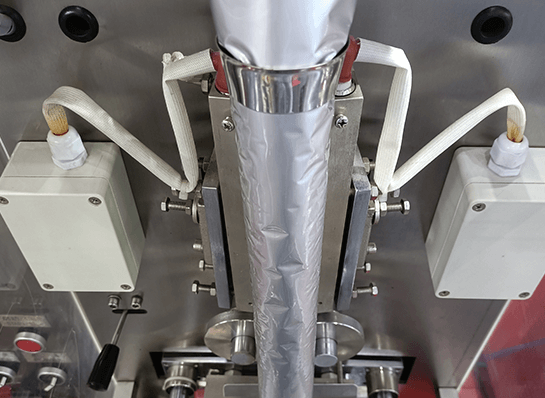 Nahaufnahme einer vertikal ausgerichteten Verpackungsmaschine mit einer Folienrolle und zwei weißen Kabeln, die zu weißen Anschlusskästen führen 