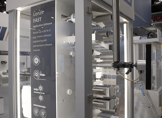 Teilansicht einer Wickelmaschine mit mehreren Rollen und einem vertikalen Schild mit Text und Symbolen zur Lenze FAST Software. 