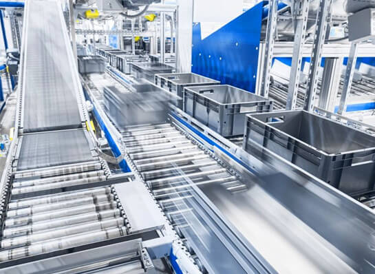 Several plastic containers are placed on a conveyor belt system in a factory environment.