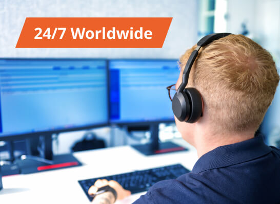 Mann mit Headset arbeitet an mehreren Monitoren, im Bild eingeblendet ein Badge mit der Aufschrift &bdquo;24/7 Worldwide".