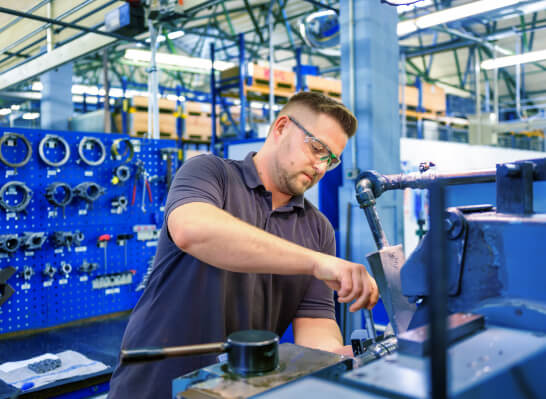 Mann mit Brille repariert ein Lenze Bauteil in einer Werkhalle mit Werkzeugwand im Hintergrund.