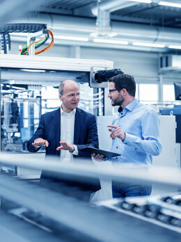Two people analyzing industrial machine with tablet in automated production environment
