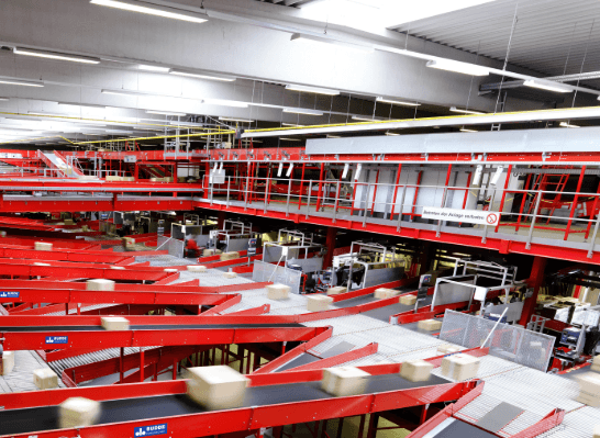 Several conveyor belts carrying packages in a large hall with red metal structures