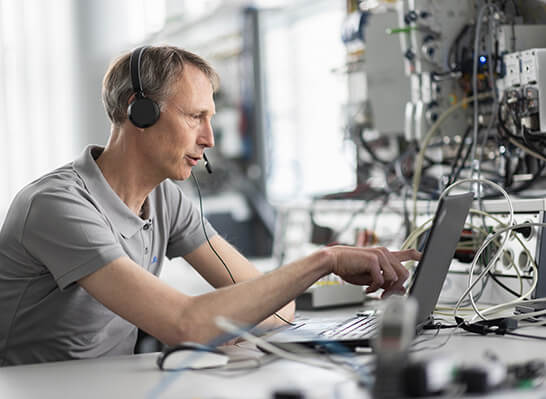 Person arbeitet an einem Laptop, Hintergrund mit Server-Racks und sichtbaren Kabeln, Umgebung eines Rechenzentrums oder Serverraums